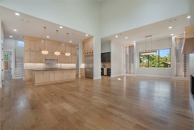 kitchen featuring light brown cabinets, hanging light fixtures, a kitchen island, a high ceiling, and light hardwood / wood-style floors