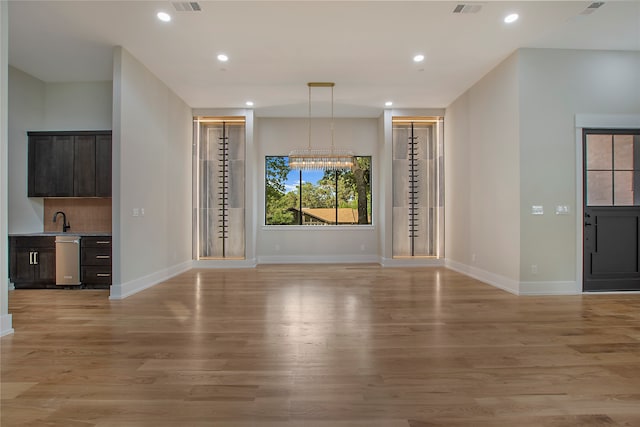 unfurnished living room featuring sink, light hardwood / wood-style flooring, and an inviting chandelier