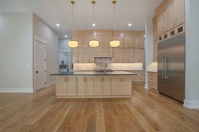 kitchen featuring built in fridge, hanging light fixtures, light hardwood / wood-style floors, light brown cabinets, and a center island with sink