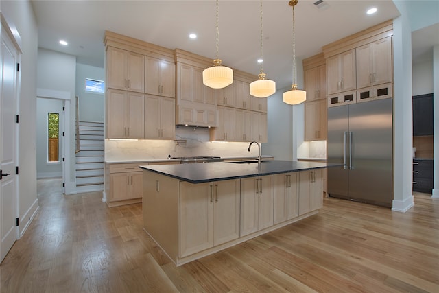 kitchen with appliances with stainless steel finishes, sink, an island with sink, hanging light fixtures, and light hardwood / wood-style floors