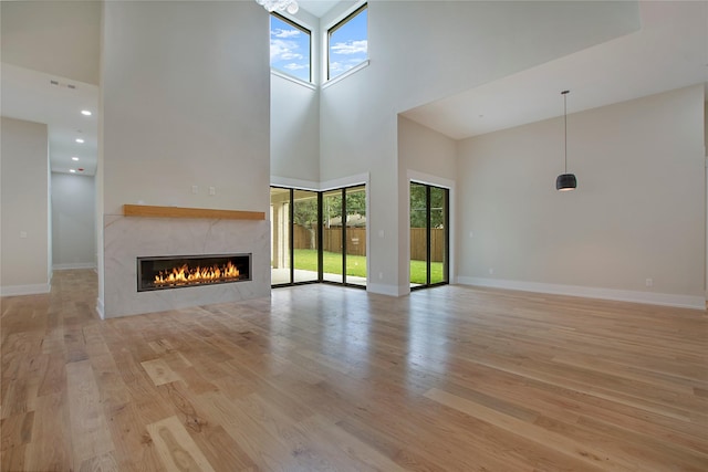 4208 Allencrest, Dallas, TX 75244 - unfurnished living room featuring a tiled fireplace, a wealth of natural light, light wood-style flooring, and a towering ceiling