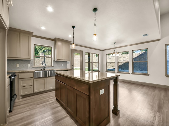 kitchen with light stone counters, a kitchen island, light hardwood / wood-style flooring, sink, and decorative light fixtures