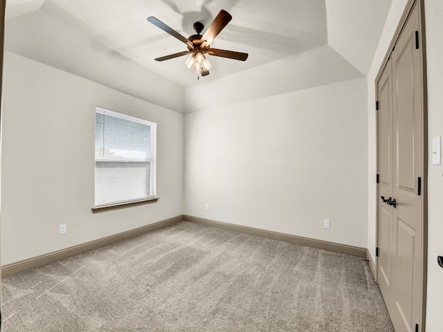 spare room featuring lofted ceiling, light colored carpet, a tray ceiling, and ceiling fan