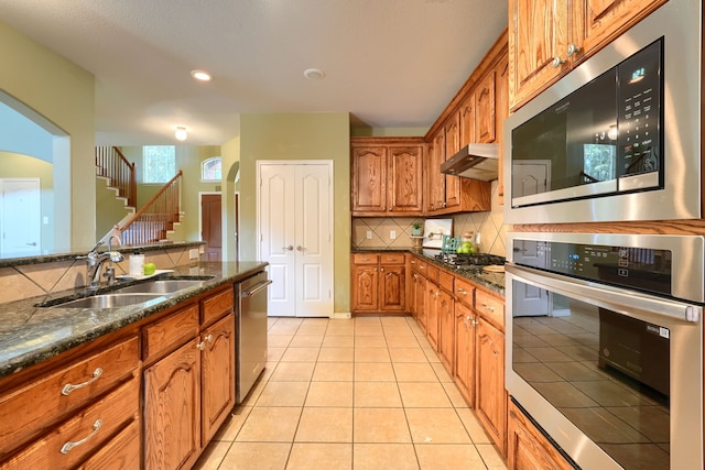 kitchen with appliances with stainless steel finishes, sink, backsplash, dark stone counters, and light tile patterned floors