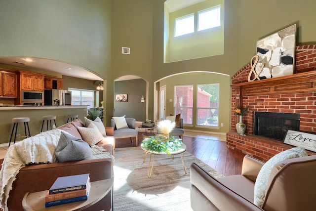 living room featuring wood-type flooring, a high ceiling, and a brick fireplace