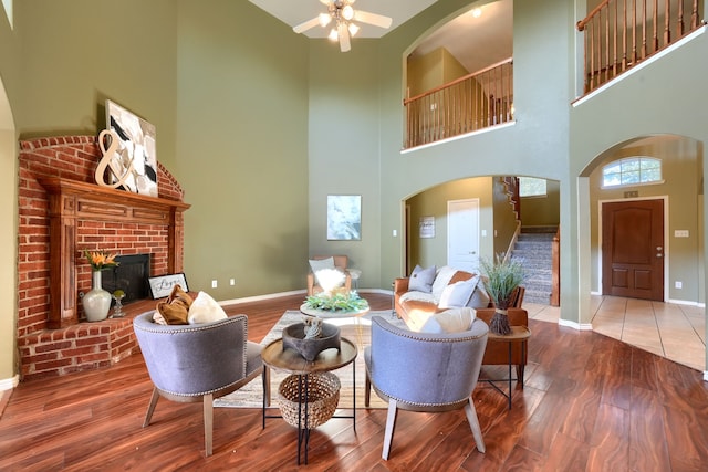 living room with a towering ceiling, hardwood / wood-style flooring, ceiling fan, and a brick fireplace