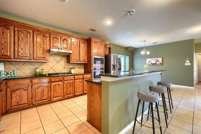 kitchen featuring light tile patterned floors, backsplash, a center island, stainless steel appliances, and decorative light fixtures