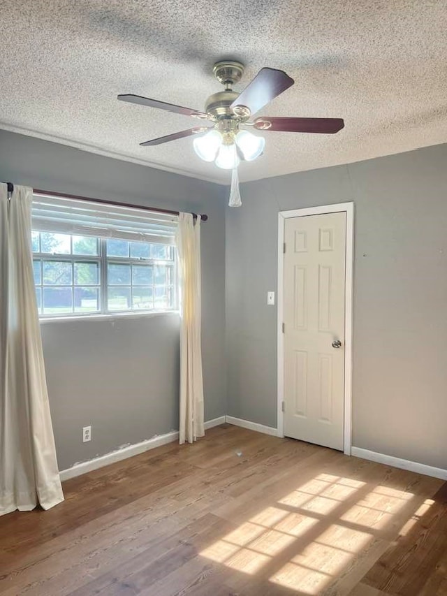 empty room with a textured ceiling, light wood-type flooring, and ceiling fan