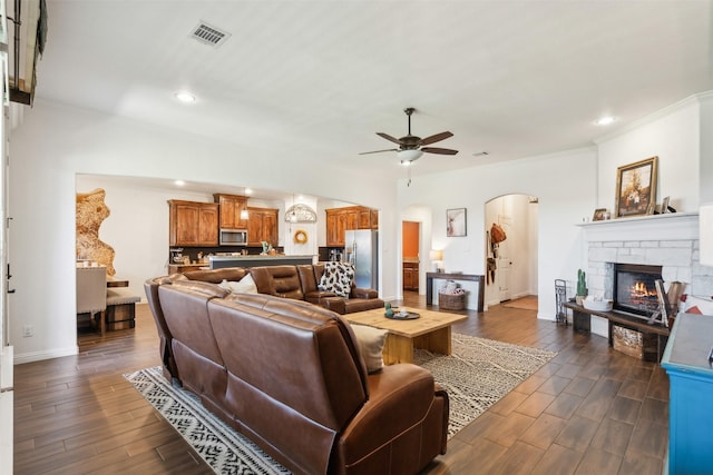 living room featuring ceiling fan, dark hardwood / wood-style flooring, crown molding, and a fireplace