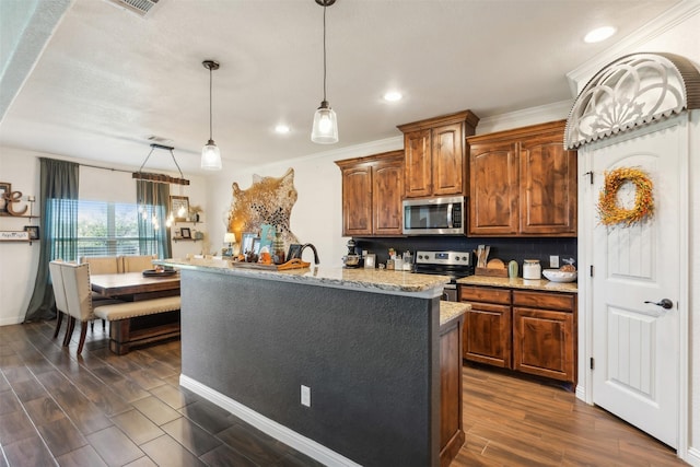 kitchen with light stone countertops, decorative light fixtures, stainless steel appliances, decorative backsplash, and a kitchen island with sink