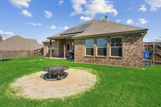 rear view of property with a patio area, an outdoor fire pit, a yard, and solar panels