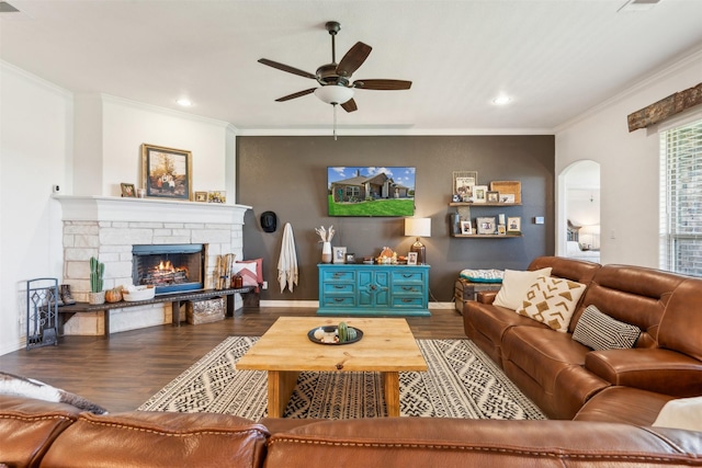 living room with crown molding, ceiling fan, dark hardwood / wood-style floors, and a stone fireplace