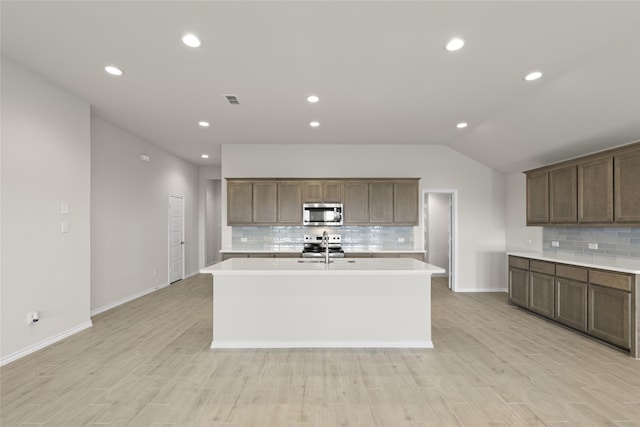 kitchen featuring tasteful backsplash, a kitchen island with sink, light hardwood / wood-style flooring, and appliances with stainless steel finishes