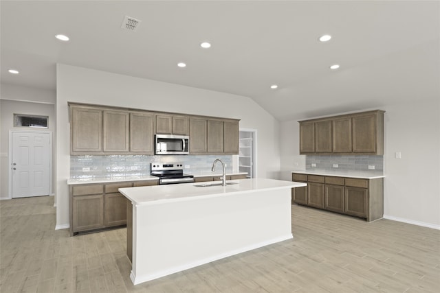 kitchen featuring sink, stainless steel appliances, backsplash, a center island with sink, and light wood-type flooring