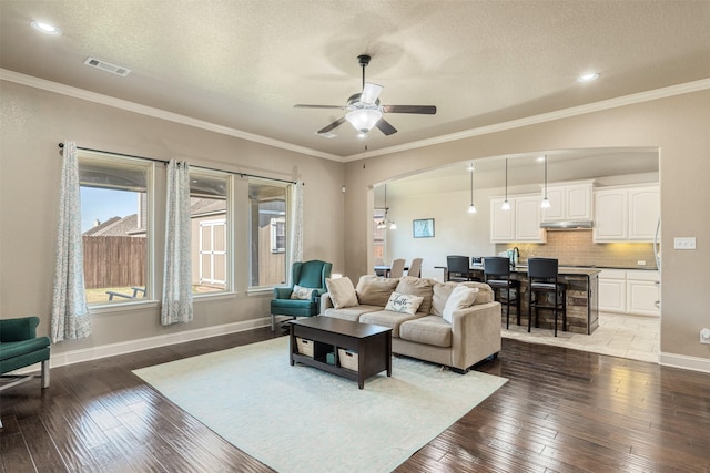 living room featuring ceiling fan, dark wood-type flooring, a textured ceiling, and ornamental molding