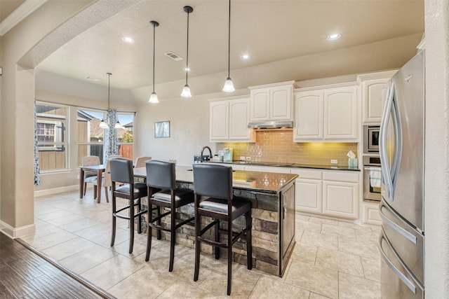 1772 Laramie Ln, Burleson, TX 76028 - kitchen with stainless steel appliances, backsplash, dark countertops, arched walkways, and under cabinet range hood