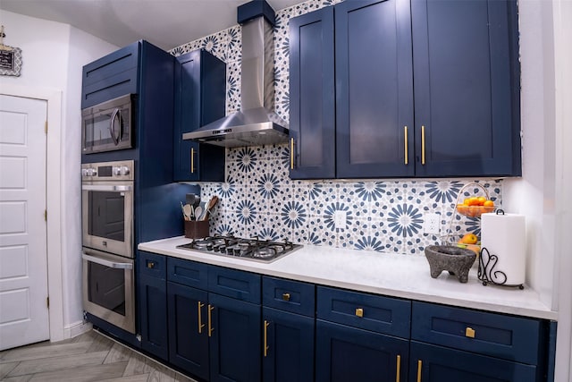 kitchen with blue cabinetry, decorative backsplash, wall chimney range hood, and stainless steel appliances