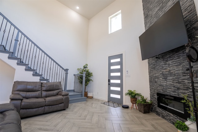 living room with a stone fireplace, light parquet floors, and a high ceiling