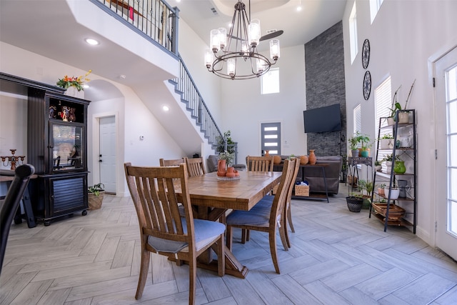 dining room featuring a healthy amount of sunlight, a fireplace, a towering ceiling, and light parquet floors