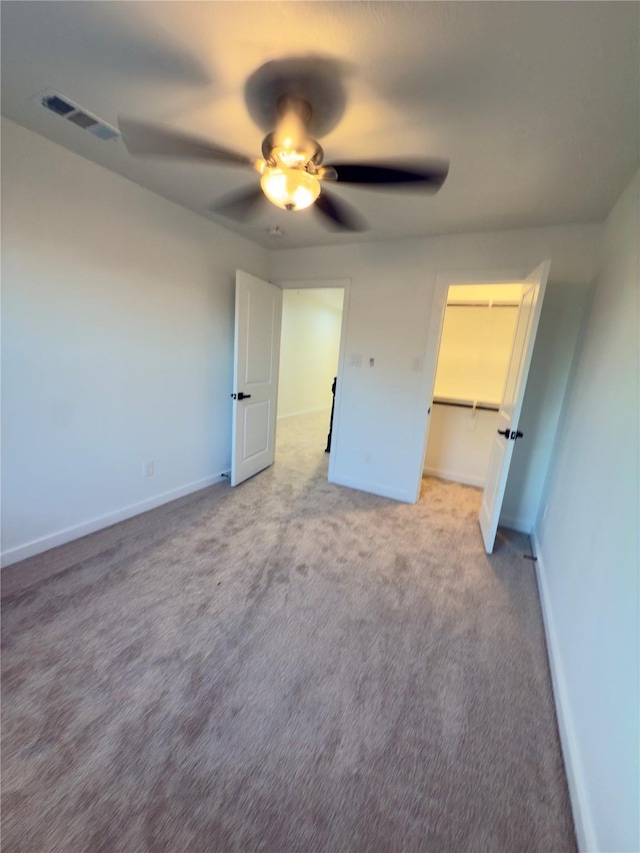 unfurnished bedroom with ceiling fan, light colored carpet, a closet, and a walk in closet