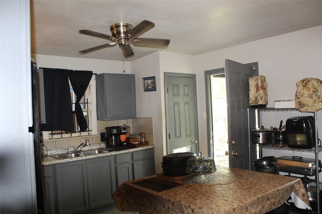 kitchen with gray cabinetry, a sink, a ceiling fan, light countertops, and decorative backsplash