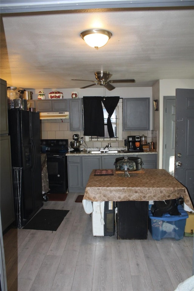 kitchen with light wood-style floors, gray cabinetry, under cabinet range hood, and black appliances