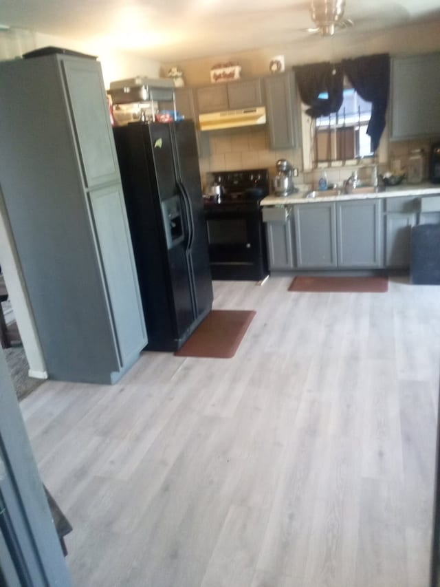 kitchen with black appliances, light wood finished floors, light countertops, and under cabinet range hood