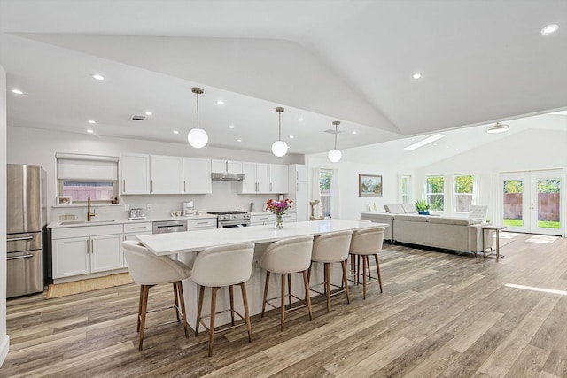 kitchen featuring lofted ceiling, appliances with stainless steel finishes, a spacious island, white cabinetry, and light hardwood / wood-style flooring