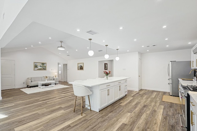 kitchen with lofted ceiling, white cabinets, hanging light fixtures, light hardwood / wood-style floors, and stainless steel appliances