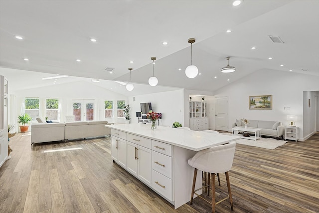 kitchen with a spacious island, hanging light fixtures, vaulted ceiling, and white cabinets