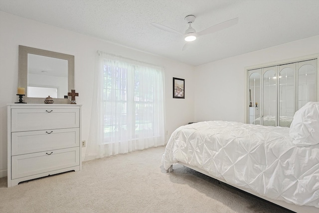 bedroom featuring a closet, a textured ceiling, light colored carpet, and ceiling fan