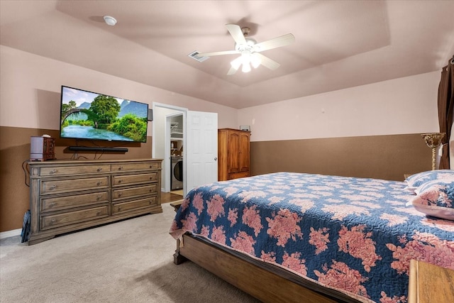 bedroom featuring washer / clothes dryer, light colored carpet, a tray ceiling, and ceiling fan