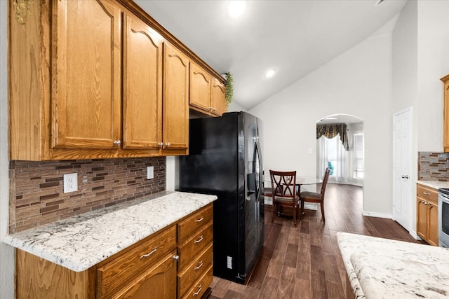 kitchen with dark wood-type flooring, black refrigerator with ice dispenser, light stone counters, high vaulted ceiling, and tasteful backsplash