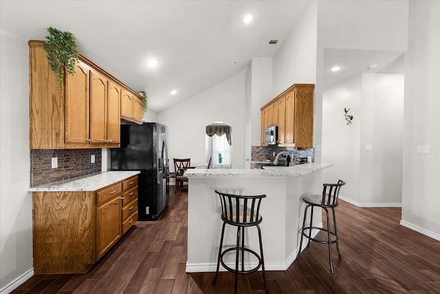 kitchen featuring light stone countertops, kitchen peninsula, stainless steel appliances, a breakfast bar area, and dark hardwood / wood-style floors