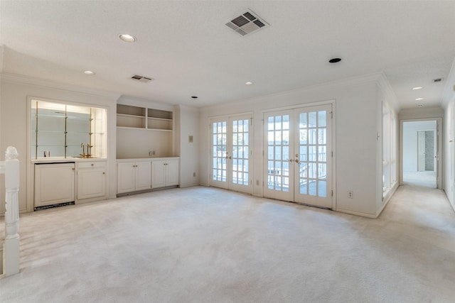 unfurnished living room featuring ornamental molding, light carpet, a textured ceiling, and french doors