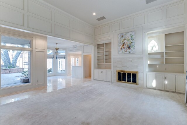 unfurnished living room featuring crown molding, light colored carpet, built in shelves, and a tile fireplace