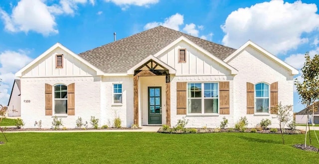 view of front of property with board and batten siding, brick siding, a shingled roof, and a front lawn