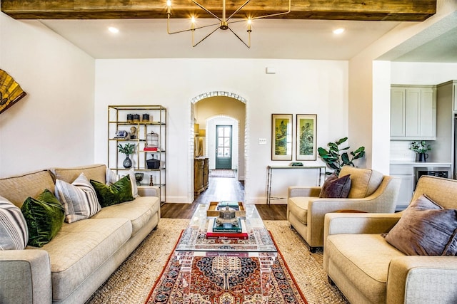 living room featuring baseboards, arched walkways, wood finished floors, beam ceiling, and a notable chandelier