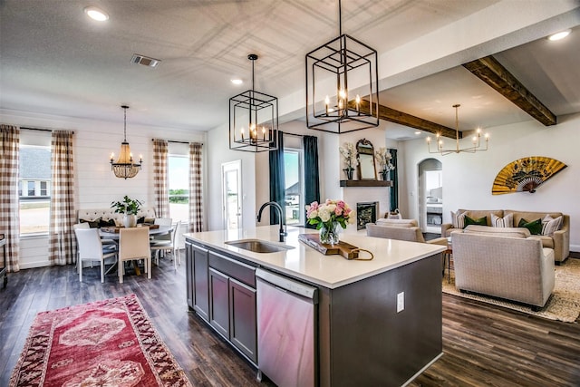 kitchen featuring stainless steel dishwasher, a kitchen island with sink, a sink, and decorative light fixtures