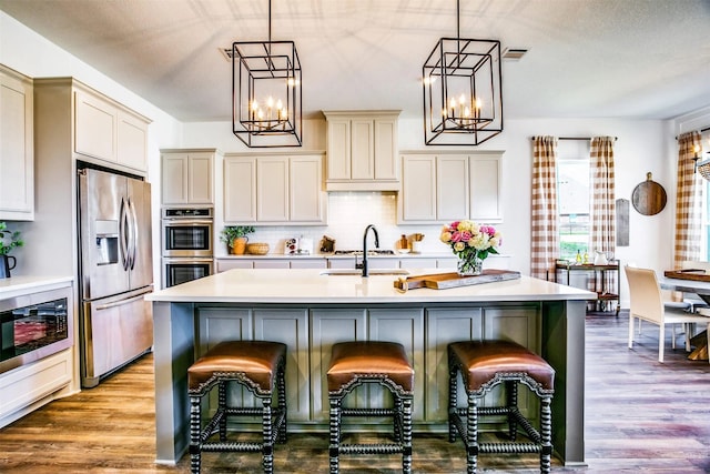 kitchen with stainless steel appliances, an island with sink, light countertops, and pendant lighting