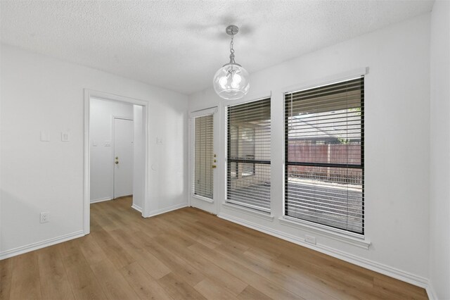 unfurnished room with light hardwood / wood-style floors, a textured ceiling, and an inviting chandelier