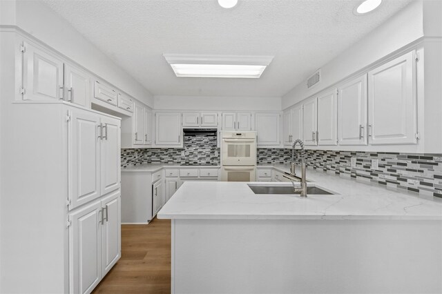 kitchen featuring kitchen peninsula, white cabinets, backsplash, wood-type flooring, and sink