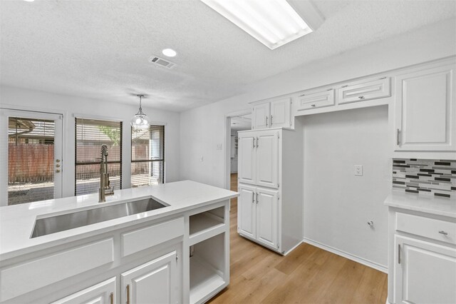 kitchen with decorative backsplash, sink, pendant lighting, white cabinets, and light hardwood / wood-style floors