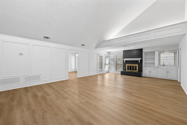 unfurnished living room featuring a textured ceiling, lofted ceiling, a brick fireplace, and light wood-type flooring