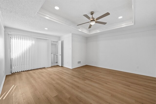 spare room with light hardwood / wood-style floors, a raised ceiling, a textured ceiling, and ceiling fan