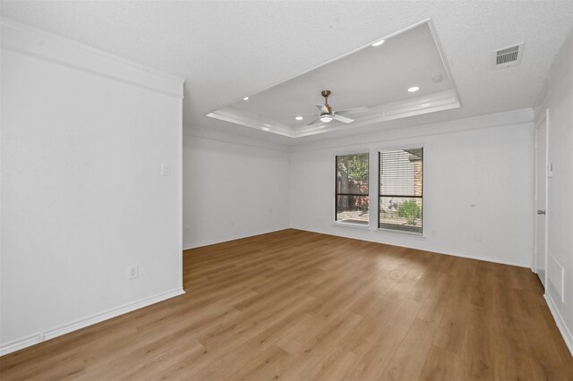 unfurnished room with ceiling fan, a textured ceiling, a tray ceiling, light wood-type flooring, and crown molding