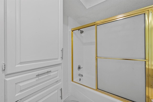 bathroom with combined bath / shower with glass door and a textured ceiling