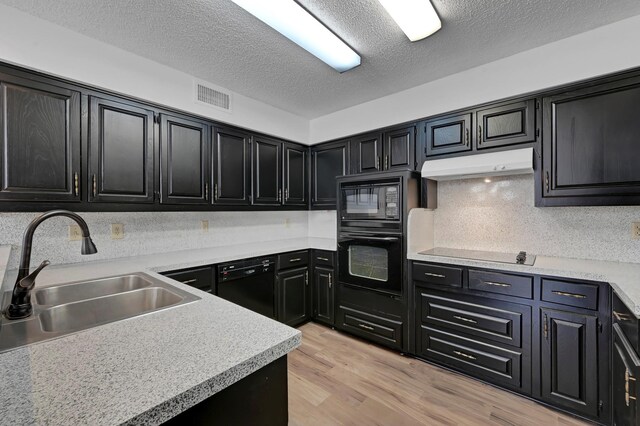 kitchen featuring decorative backsplash, a textured ceiling, light wood-type flooring, black appliances, and sink