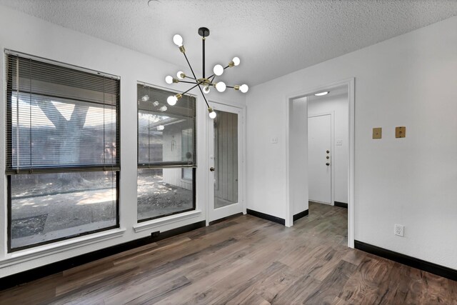 unfurnished dining area with a textured ceiling, a chandelier, and dark hardwood / wood-style floors