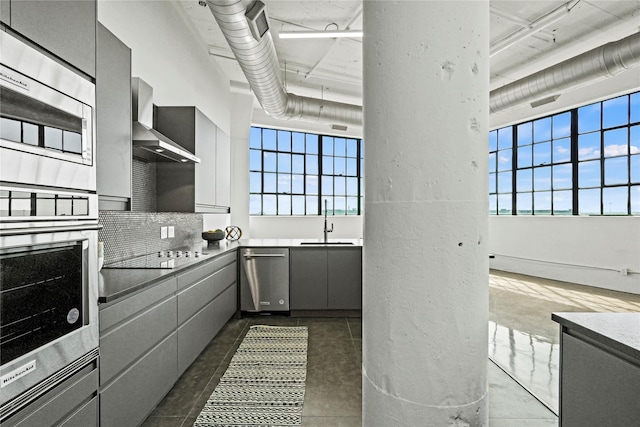 kitchen with appliances with stainless steel finishes, tasteful backsplash, sink, gray cabinetry, and wall chimney range hood